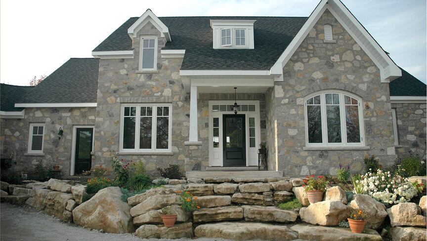 Custom multi-pane architectural windows and a dark front door on a luxury stone home facade.