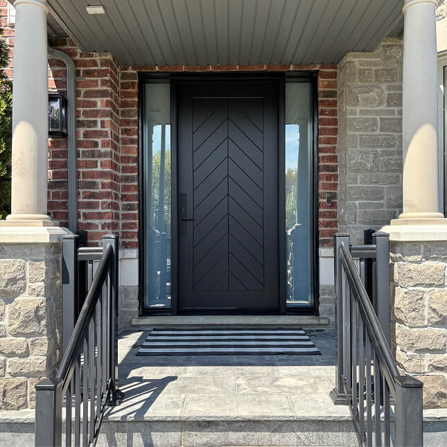 Modern black front door with a chevron panel pattern, tall glass sidelights, brick and stone framing.