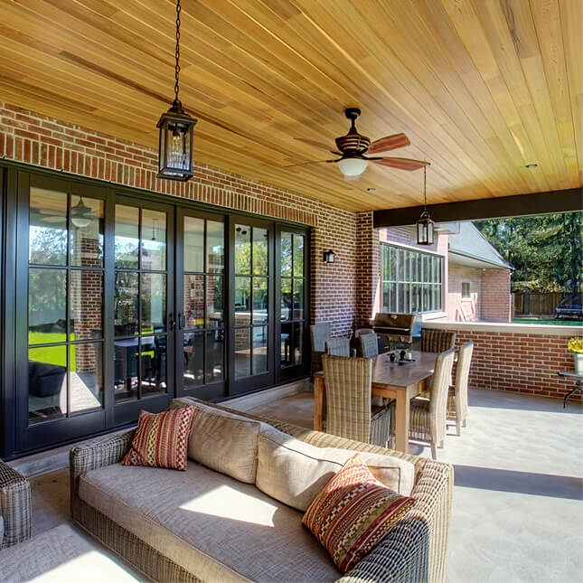 Covered brick patio with black framed glass doors, a wood-panelled ceiling and outdoor living space.
