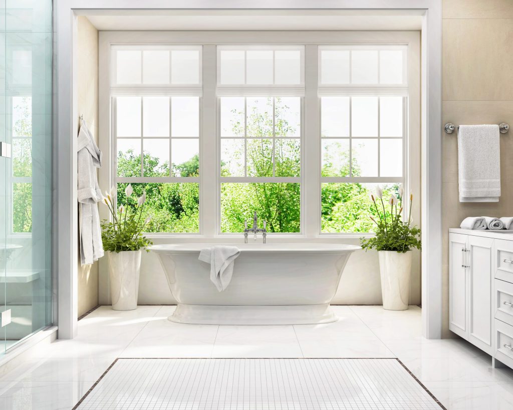 Bright bathroom with three white multi-pane windows above a freestanding bathtub.