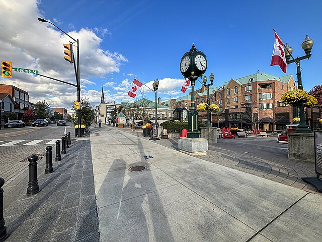 Oakville downtown streetscape with a clock tower, Canadian flags, storefronts, brick buildings, and sidewalk planters