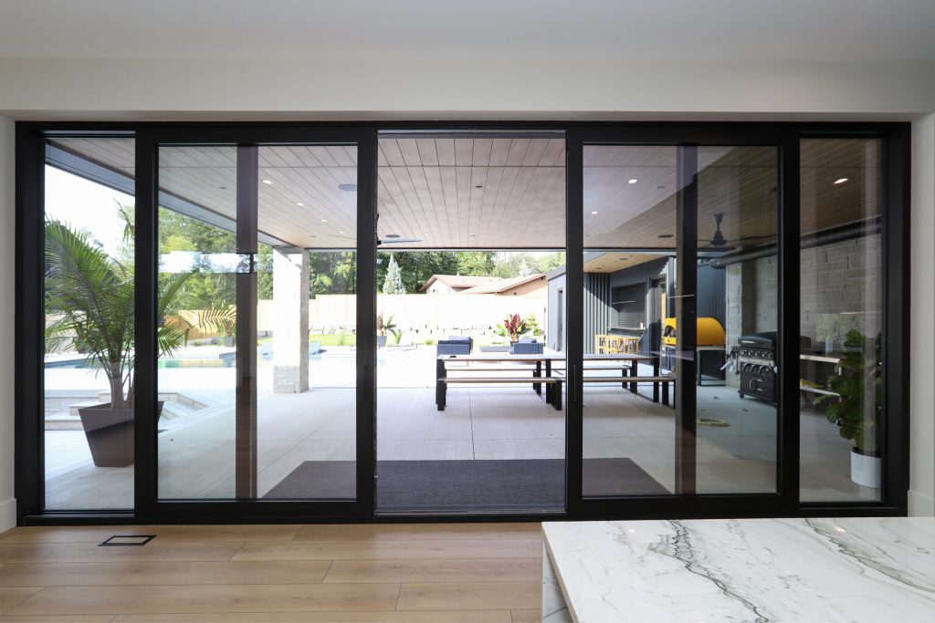 Black aluminum sliding glass doors opening onto a bright patio and pool