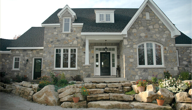 Stone home with custom white windows and a dark front entry door.